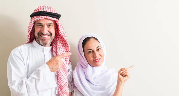 Middle age arabic couple, woman and man very happy pointing with hand and finger to the side