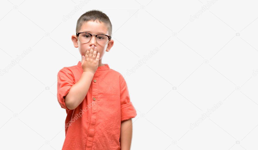 Dark haired little child wearing glasses cover mouth with hand shocked with shame for mistake, expression of fear, scared in silence, secret concept