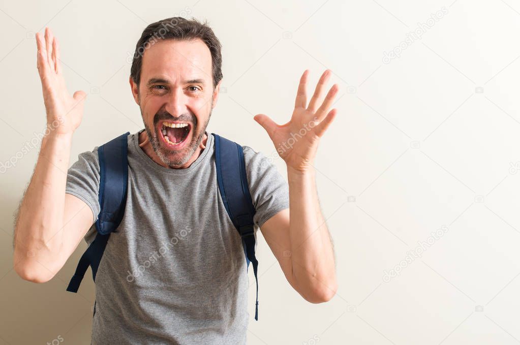 Senior man using backpack very happy and excited, winner expression celebrating victory screaming with big smile and raised hands