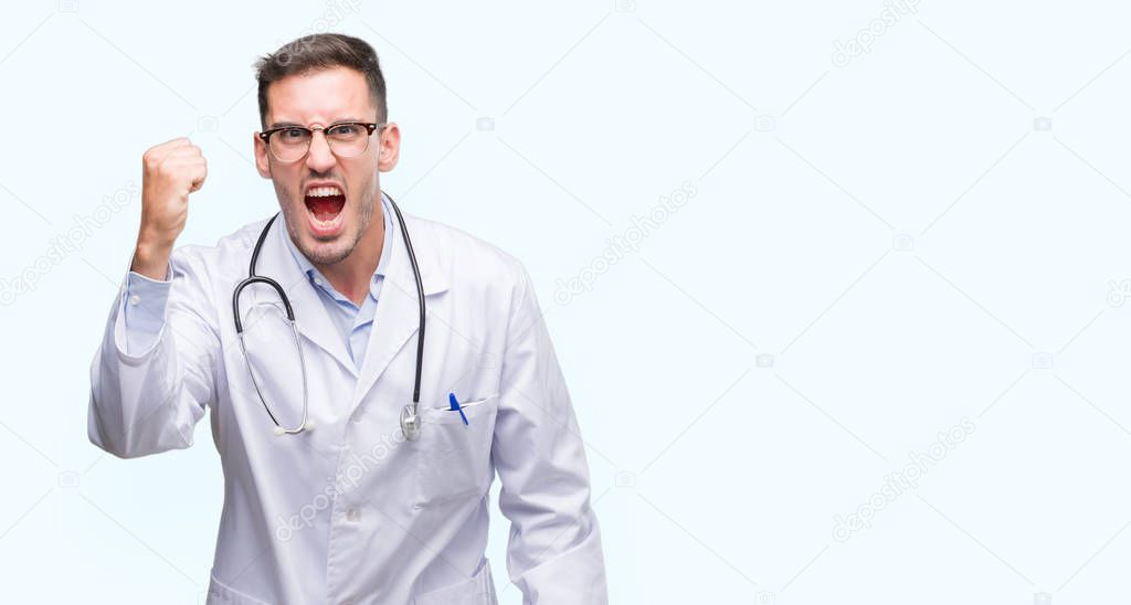 Handsome young doctor man angry and mad raising fist frustrated and furious while shouting with anger. Rage and aggressive concept.