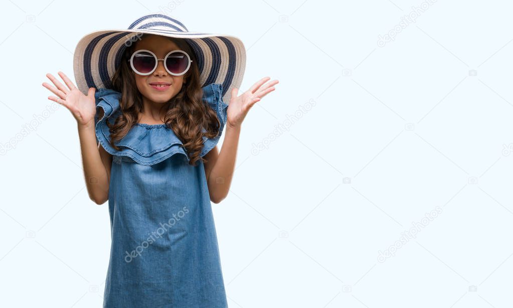 Brunette hispanic girl wearing sunglasses and summer hat very happy and excited, winner expression celebrating victory screaming with big smile and raised hands