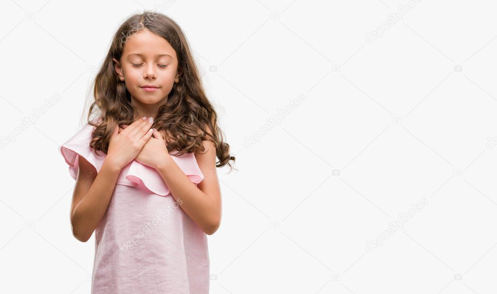 Brunette hispanic girl wearing pink dress smiling with hands on chest with closed eyes and grateful gesture on face. Health concept.
