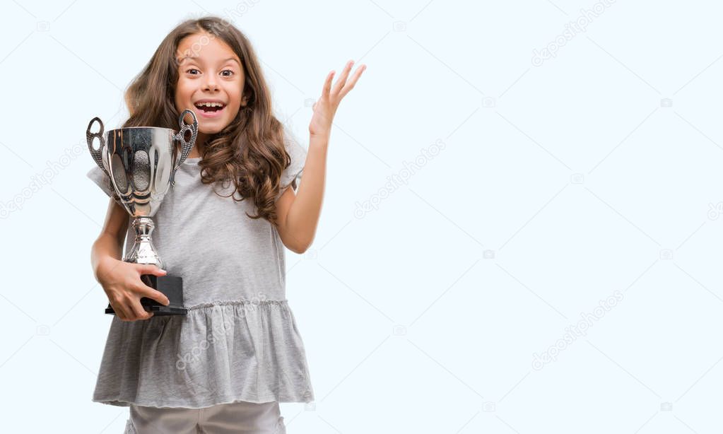 Brunette hispanic girl holding a trophy very happy and excited, winner expression celebrating victory screaming with big smile and raised hands