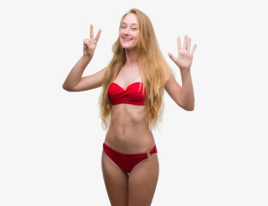 Gösterilen ve parmakları ile işaret kırmızı bikini giyen sarışın genç kadın kendinden emin ve mutlu gülümseyerek süre yedi numara.