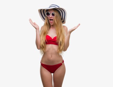 Bikini, güneş gözlüğü ve çok mutlu ve heyecanlı, yaz şapka giymiş sarışın genç kadın kazanan ifade büyük gülümseme ile çığlık ve ellerini kaldırdı zaferini kutluyor