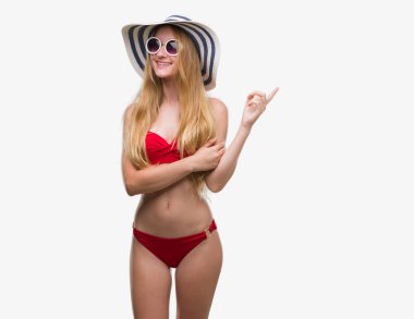 Bikini, güneş gözlüğü ve el ve parmak ile tarafına işaret çok mutlu yaz şapka giymiş sarışın genç kadın