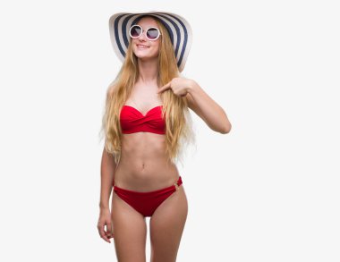 Bikini, güneş gözlüğü ve kendisi için sürpriz yüz işaret parmağı ile yaz şapka giymiş sarışın genç kadın