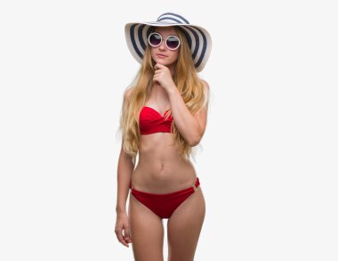Bikini, güneş gözlüğü ve yaz şapka ciddi bir yüz düşünme hakkında soru, çok karışık fikir giymiş sarışın genç kadın