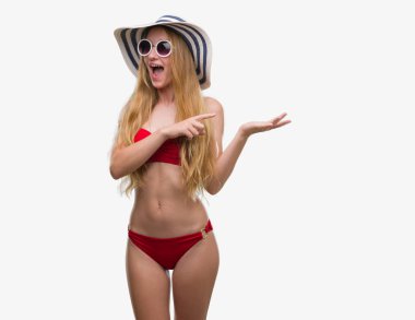 Bikini, güneş gözlüğü ve el ve parmak ile işaret çok mutlu yaz şapka giymiş sarışın genç kadın