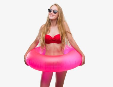 Ayakta ve diş gösterilen kendine güvenen bir gülümsemeyle gülümseyerek mutlu bir yüz ile bikini ve holding pembe flatör giymiş sarışın genç kadın