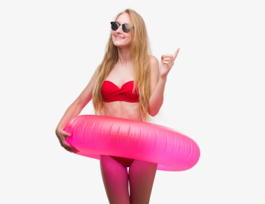 Bikini ve holding pembe flatör el ve parmak ile tarafına işaret çok mutlu giymiş sarışın genç kadın