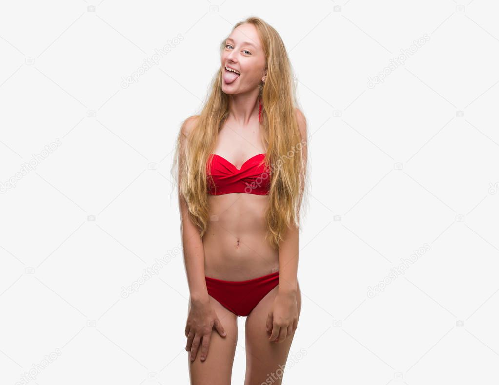 Blonde teenager woman wearing red bikini sticking tongue out happy with funny expression. Emotion concept.