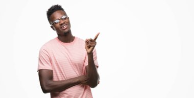 Kameraya bakarak yan el ve parmak ile işaret, yüzünde kocaman bir gülümseme ile pembe t-shirt giyen genç Afro-Amerikan adam.