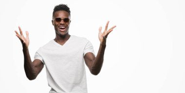 Kocaman bir gülümseme ile çığlık zaferini kutluyor ve ellerini kaldırdı güneş gözlüğü çok mutlu ve heyecanlı, kazanan ifade giyen genç Afro-Amerikan adam