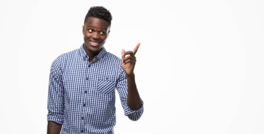 Kameraya bakarak yan el ve parmak ile işaret, yüzünde kocaman bir gülümseme ile mavi gömlek giymiş genç Afro-Amerikan adam.