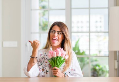 Genç kadın evde el ve parmak ile yukarı dönük mutlu yüz gülümseyen ile pembe Lale çiçek tutan