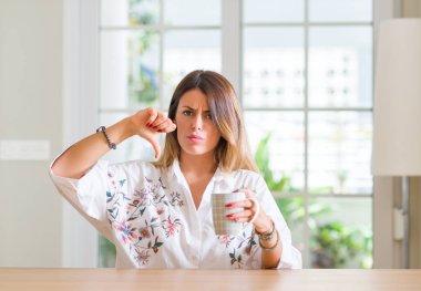 Genç kadın evde antipati başparmak aşağı, ret kavramı ile gösterilen işareti negatif kızgın yüz, kahve içme