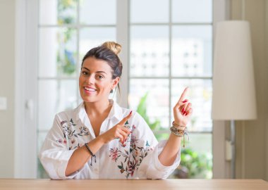 Genç kadın evde gülümseyen ve iki elleri ve parmakları ile tarafına işaret kamera bakıyor.