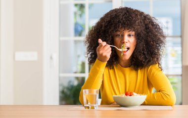 Afrikalı-Amerikalı kadın evde acımak yüz ciddi düşünüyorum üstünde kendine güvenen bir ifade ile makarna salatası yemek