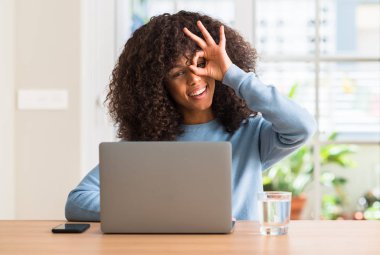 Mutlu yüz el parmaklarının arasından seyir göz üzerinde ok işaretiyle yapıyor gülümseyen ile evde dizüstü bilgisayar kullanan Afrikalı-Amerikalı kadın