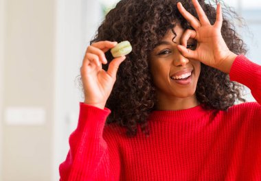 Macaron el parmaklarının arasından seyir göz üzerinde ok işaretiyle yapıyor gülümseyen mutlu yüz tutan Afrikalı-Amerikalı kadın