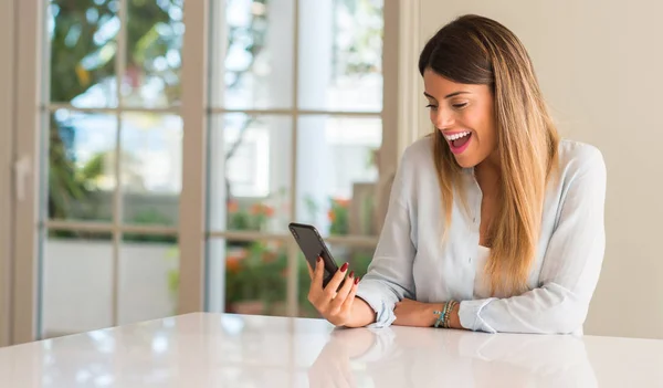 若い女性の幸せな笑顔のスマート フォンを使用して 家庭で見ている携帯電話を保持しています — ストック写真