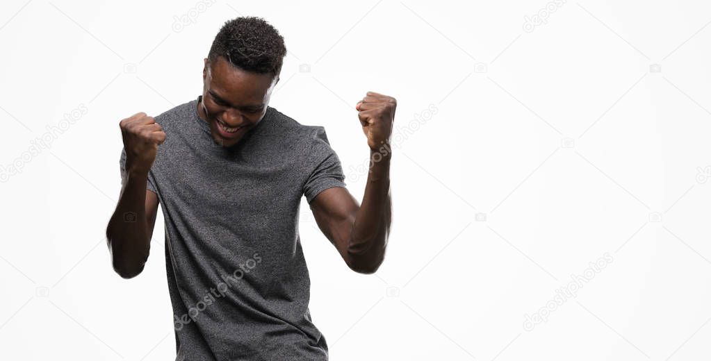 Young african american man wearing grey t-shirt very happy and excited doing winner gesture with arms raised, smiling and screaming for success. Celebration concept.