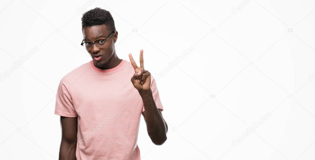 Young african american man wearing pink t-shirt showing and pointing up with fingers number two while smiling confident and happy.