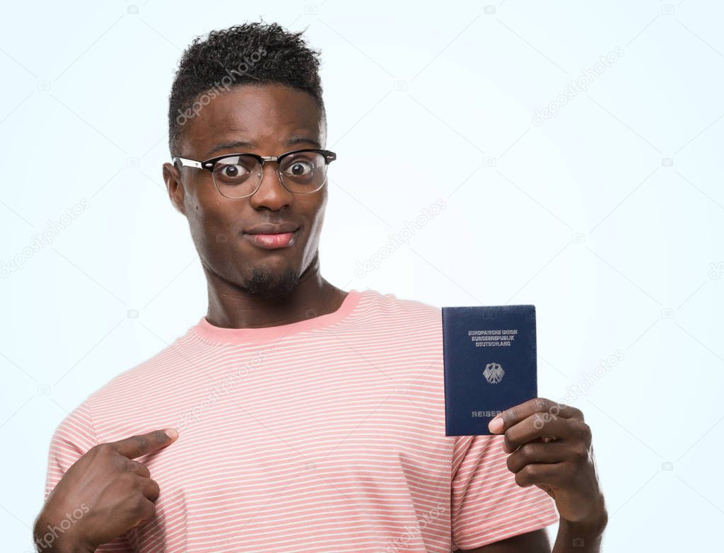 Young african american man holding german passport with surprise face pointing finger to himself