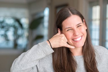 Genç güzel kadın evde gülümseyen el ve parmak telefonda konuşmak ile telefon jest yapıyor. Kavramları iletişim.