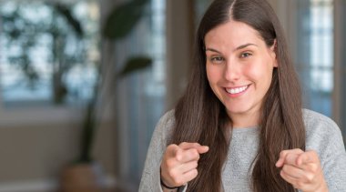 Genç güzel kadın evde fotoğraf makinesi ile mutlu ve komik yüz için parmakları işaret. İyi enerji ve vibes.