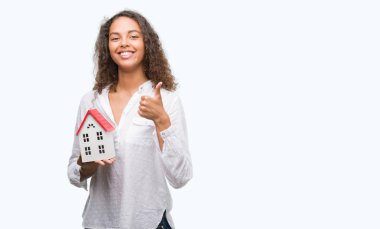 Küçük ev mutlu ile büyük tutan genç İspanyol gerçek durum Aracısı kadın gülümseme ok işareti, başparmak ile parmak, mükemmel işareti yapıyor