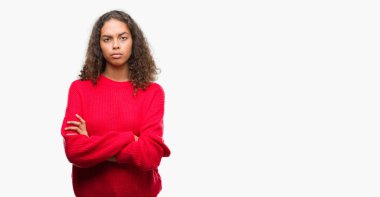 Çapraz kolları olan yüzündeki kırmızı kazaklı şüpheci ve sinir, onaylamayan ifade giyen genç İspanyol kadın. Negatif kişi.