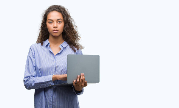 Young hispanic woman holding computer laptop with a confident expression on smart face thinking serious