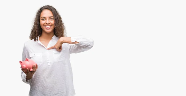 Junge Hispanische Frau Hält Sparschwein Mit Überraschendem Gesicht Und Zeigt — Stockfoto