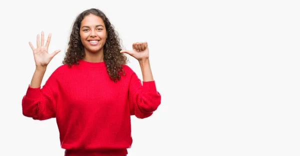 指で上向きの表示と赤いセーターを着ている若いヒスパニック女性ナンバー 自信を持って 幸せな笑みを浮かべて — ストック写真