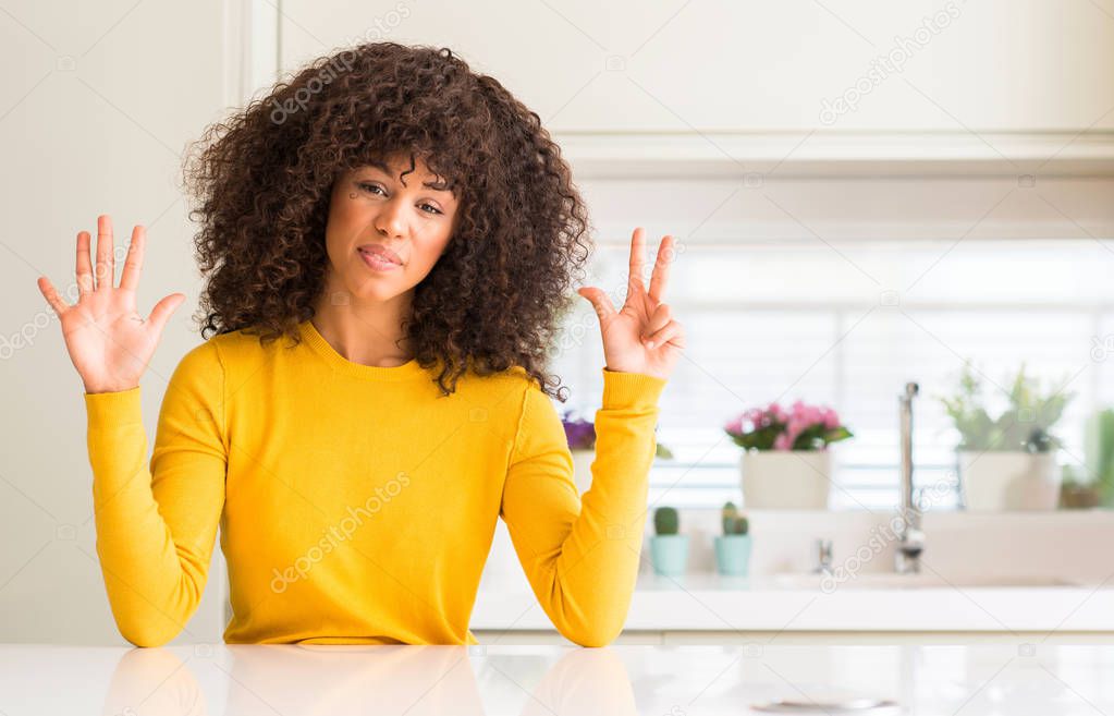African american woman wearing yellow sweater at kitchen showing and pointing up with fingers number eight while smiling confident and happy.