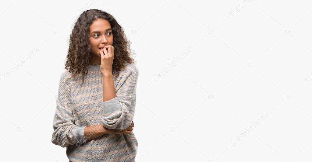 Beautiful young hispanic woman wearing stripes sweater looking stressed and nervous with hands on mouth biting nails. Anxiety problem.