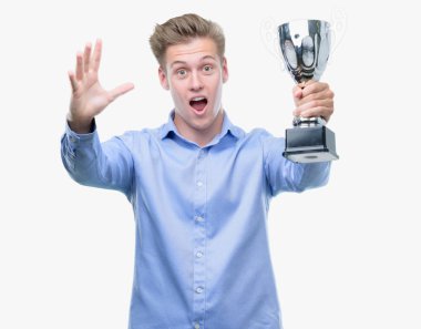 Genç yakışıklı sarışın adam büyük gülümseme ile çığlık zaferini kutluyor ve ellerini kaldırdı bir kupa çok mutlu ve heyecanlı, kazanan ifade holding