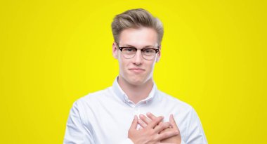 Genç yakışıklı sarışın adam ile gülümseyen gözlerin kapalı ve yüzünde minnettar jest ile göğüs üzerinde eller. Sağlık kavramı.