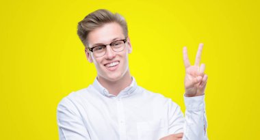 Mutlu yüz zafer işareti yaparken kameraya göz kırpıyor ile gülümseyen genç yakışıklı sarışın adam. İki numaralı.