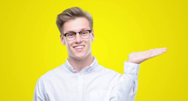 Genç yakışıklı sarışın adam gülümseyen neşeli sunulması ve kameraya bakarak avucunun ile işaret.