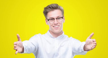 Sarılmak için kollarını açarak gülümseyerek kameraya bakarak genç yakışıklı sarışın adam. Neşeli ifade kucaklayan mutluluk.