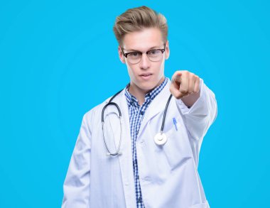 Genç yakışıklı sarışın doktor kamera ve size, el işareti, pozitif ve kendinden emin bir jest ön parmak ile işaret