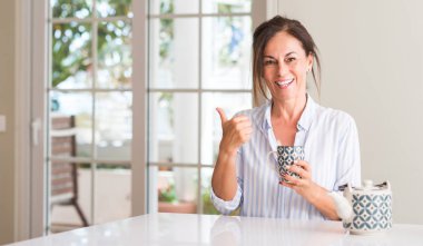 Bir fincan çay ya da kahve el ve mutlu yüz gülümseyen parmak ile işaret içme orta yaşlı kadın