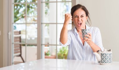 Bir fincan çay ya da kahve rahatsız ve öfke, çılgın ve yükseltilmiş el, öfke kavramı ile diye bağıran ile sinirli bağırarak içme kadın orta yaşlı