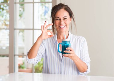 Orta yaşlı kadın içme milkshake bardakta parmak, mükemmel sembolü ile ok işareti yapıyor