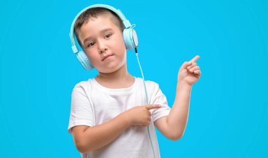 Koyu saçlı küçük çocuk müzik dinleme kulaklıklarla el ve parmak ile tarafına işaret çok mutlu
