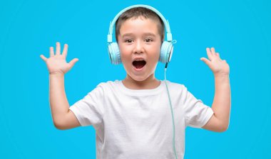 Kocaman bir gülümseme ile çığlık zaferini kutluyor kulaklıklar çok mutlu ve heyecanlı, kazanan ifade ile müzik dinleme ve ellerini kaldırdı koyu saçlı küçük çocuk