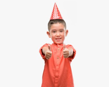 Koyu saçlı küçük çocuk Doğum günü mutlu ok işareti, başparmak ile parmak, mükemmel işareti yapıyor kocaman bir gülümseme ile şapkası